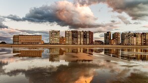 A waterfront hotel with multiple high-rise buildings, a reflective water surface, and a cloudy sky. - Westend Palace (Middelkerke)