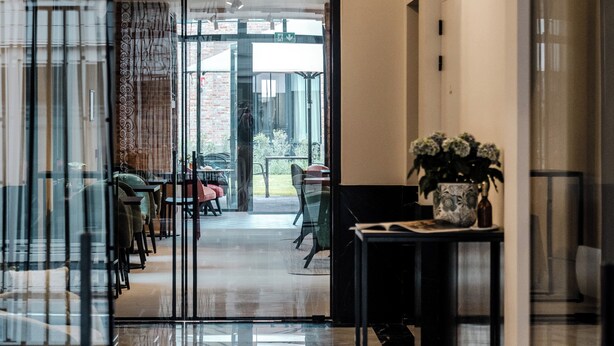 Un moderno vestíbulo de hotel con un separador de vidrio, piso de mármol y una zona de estar con mesas y sillas.