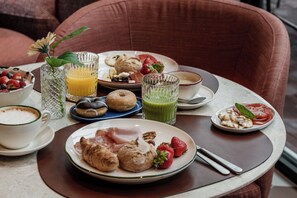 A breakfast setting with various dishes, including pastries, fruits, and beverages on a table.