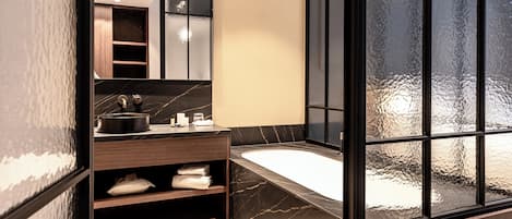 A modern bathroom with a large mirror, dark marble countertop, and a glass-enclosed bathtub.
