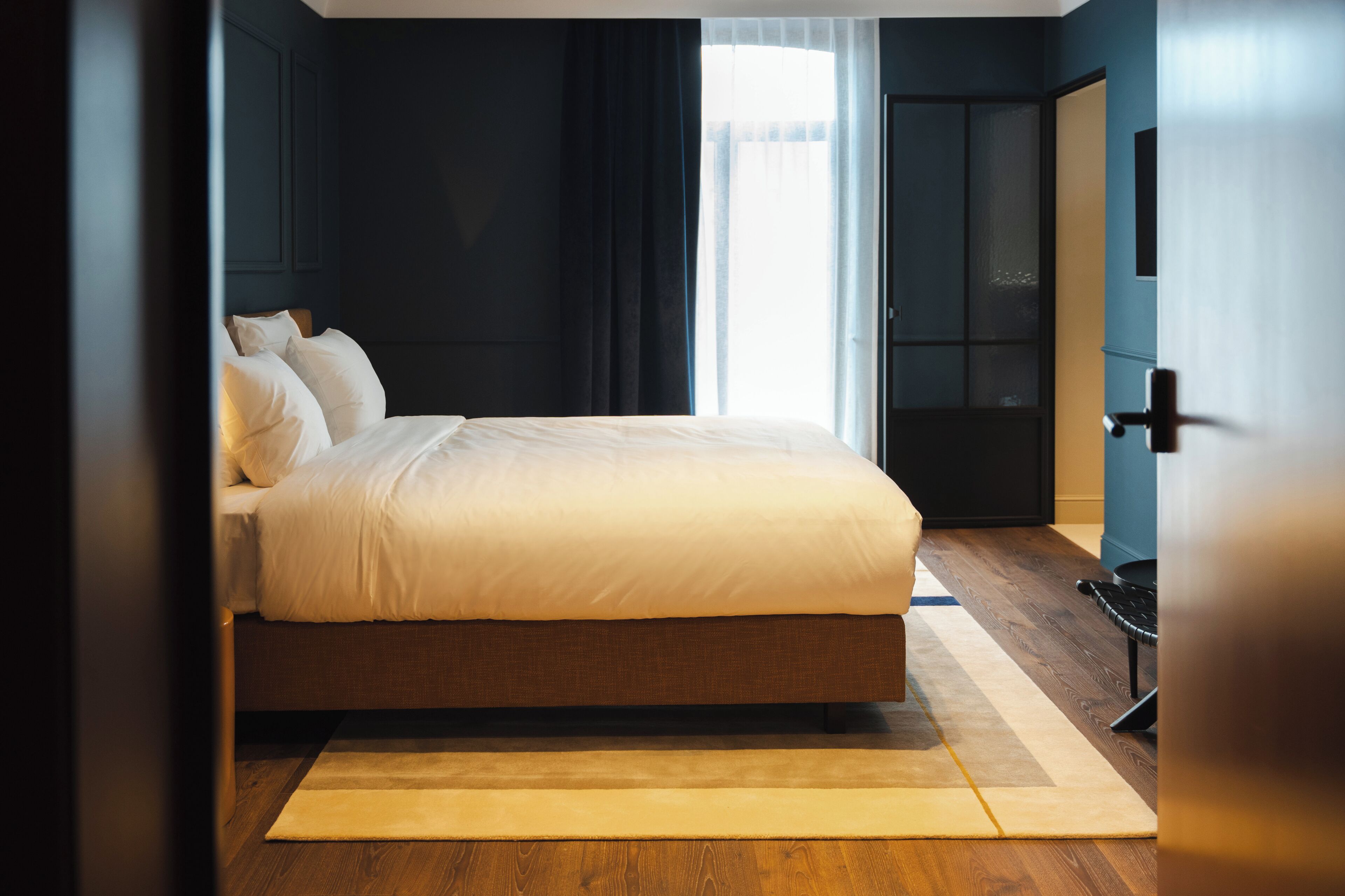 A modern bedroom with a large bed, dark walls, and a wooden floor.