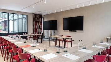 A conference room with a long table, red chairs, and two large screens on the walls.