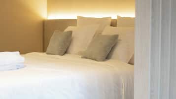 A neatly made bed with white linens and a brown accent rug, a headboard, and a wall-mounted light fixture.