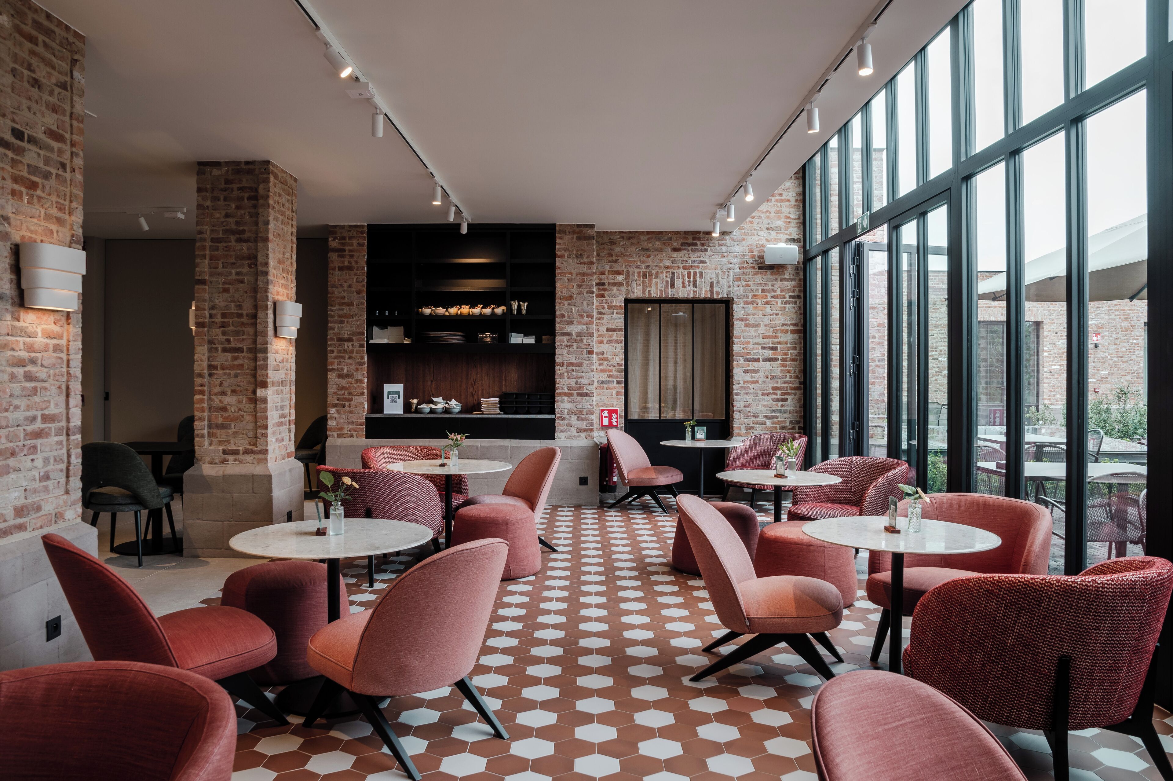 A modern cafe with brick walls, large windows, and red upholstered chairs.