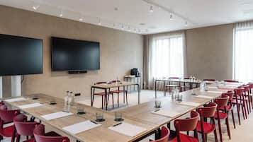 Ett konferensrum med ett långt bord, röda stolar, en platt-TV och ett stort fönster med gardiner.