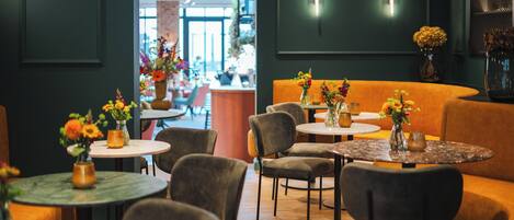 A restaurant interior with round tables, cushioned seating, and floral centerpieces.