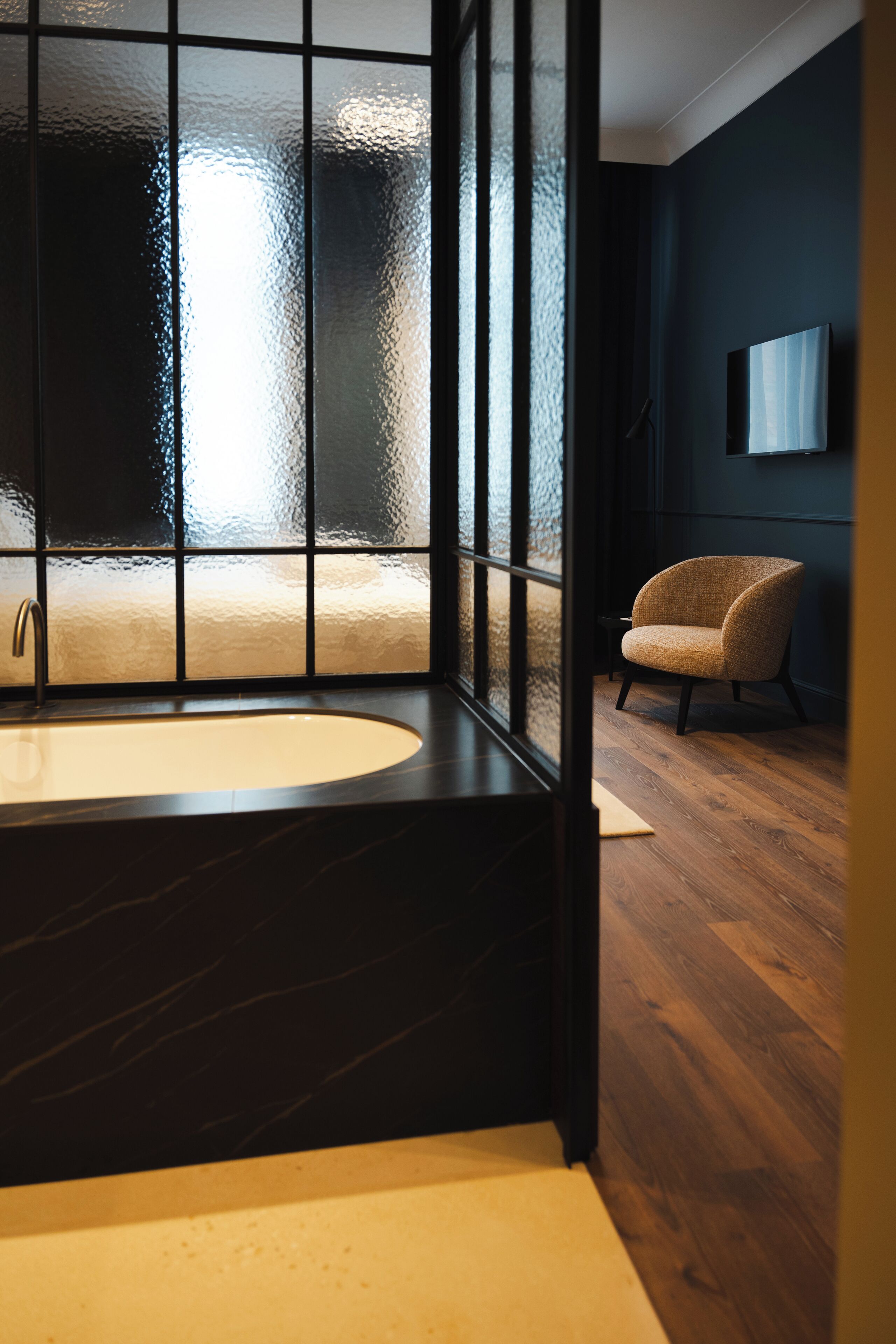 Un baño moderno con una bañera grande, piso de madera y una silla.