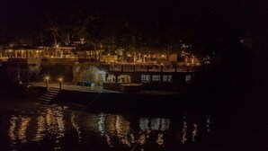 Ein Anwesen am Wasser mit Anlegesteg, einer großen Felsformation und einem mehrstöckigen Gebäude mit Balkonen.