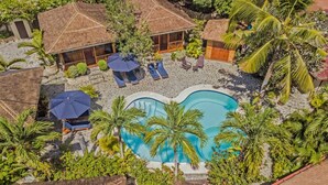 Eine Vogelperspektive zeigt einen Urlaubsort mit einem Swimmingpool, umgeben von Palmen und Liegestühlen.
