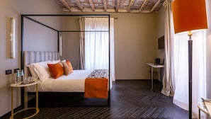 A modern hotel room with a four-poster bed, a small bedside table, a floor lamp, and a television. - The Couper Colonna (Rome)