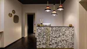 A reception desk with a marble top, a laptop, and a vase with candles. There are three pendant lights above the desk. - The Couper Colonna (Rome)
