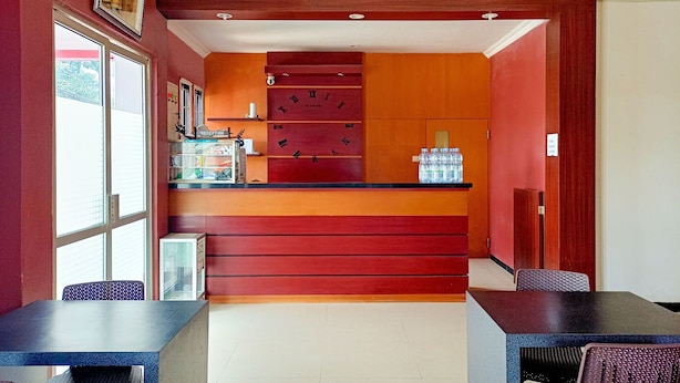 A reception area with a red and orange color scheme, a reception desk, a clock, and a window with blinds. - Hotel O Lima Dara (Tanjung Selor)