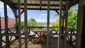A wooden deck with a table and chairs, overlooking a scenic view with palm trees and a distant landscape. - Bellevue Tamarin (Tamarin)