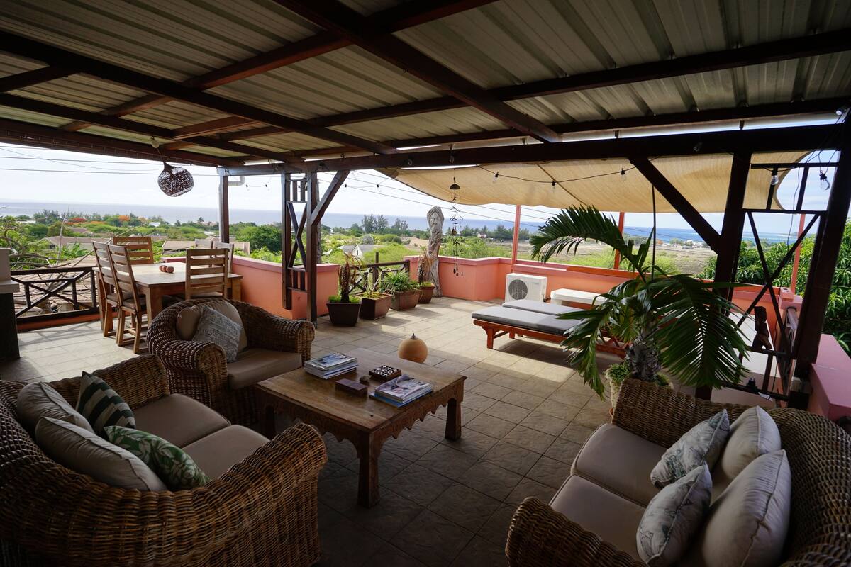 A covered patio area with wicker furniture, a wooden table, and potted plants.