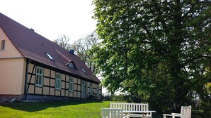 A traditional half-timbered house with a sloped roof and a water tank on the roof. There are two white wooden benches in front of the house. - Large vacation apartment in an old pastorate with fireplace and garden (Borrentin)
