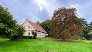 A traditional half-timbered house with a red roof, surrounded by a well-maintained lawn and a large tree. - Large vacation apartment in an old pastorate with fireplace and garden (Borrentin)