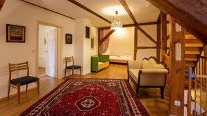 A cozy room with a wooden ceiling, a bed, a green chair, a patterned rug, and a staircase. - Large vacation apartment in an old pastorate with fireplace and garden (Borrentin)
