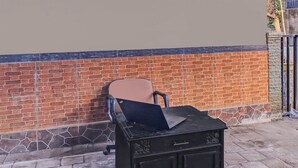 Un mueble negro con una computadora portátil encima, una silla y un muro de ladrillo.