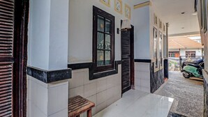 Un pasillo con suelo de baldosas, un banco de madera, una puerta con ventana y una lámpara fijada a la pared.
