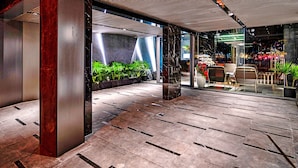 Un hall d’entrée moderne avec un sol carrelé, une grande colonne et un espace détente comprenant des fauteuils et des plantes en pot.