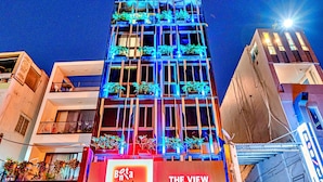 Un hôtel à la façade moderne, doté de balcons ornés de plantes et d’une enseigne indiquant « The View ».