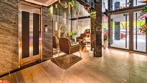 Un hall d’entrée moderne avec un mur en pierre, un comptoir d’accueil, un espace salon et une vue sur la rue.