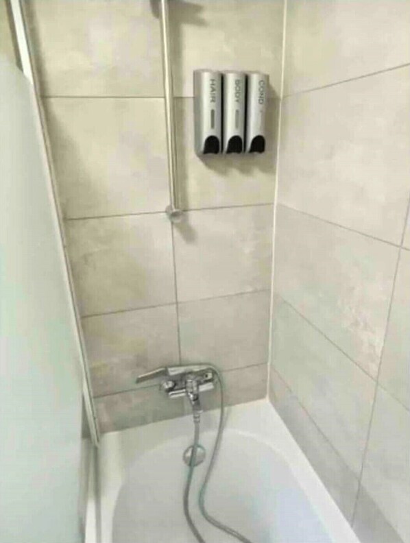 A bathroom with a bathtub, a shower, and three bottles of shampoo and conditioner on the wall. - Rosa House (Darlington)