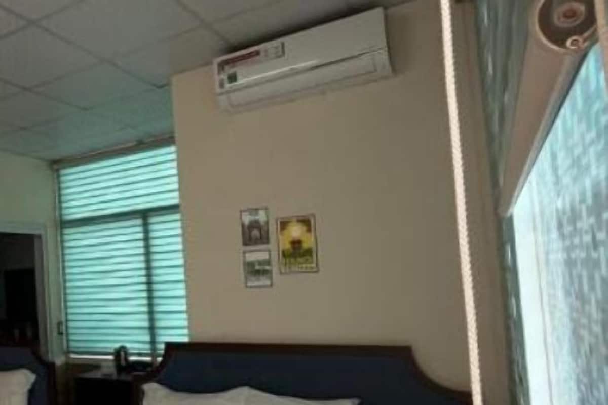 A hotel room with a bed, an air conditioning unit, a window with blinds, and a wall-mounted picture.