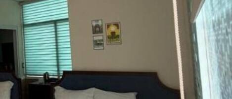 A hotel room with a bed, an air conditioning unit, a window with blinds, and a wall-mounted picture.