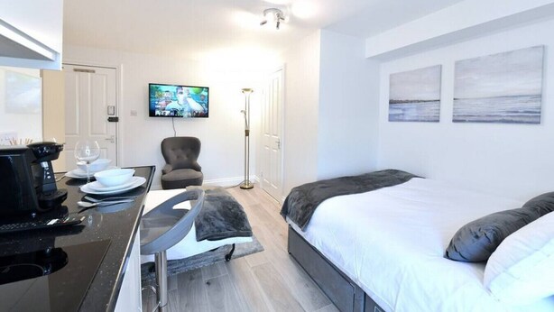 Una habitación de hotel con cama, escritorio con cafetera, silla y televisor montado en la pared.