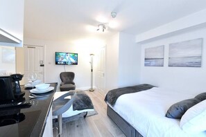 Hotellihuone, jossa on sänky, työpöytä, kahvinkeitin, tuoli ja seinälle asennettu televisio.