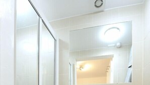 Une salle de bain avec une douche à parois de verre, un lavabo blanc avec un miroir au-dessus et des toilettes blanches.