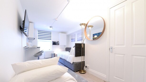 Une chambre à coucher moderne avec un lit, une table de chevet, une télévision et un grand miroir.