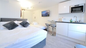 Une chambre d’hôtel moderne dotée d’un grand lit, de deux tables de chevet, d’une kitchenette équipée d’un four à micro-ondes et d’un téléviseur fixé au mur.