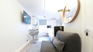 Un salon moderne avec un canapé gris, un téléviseur à écran plat fixé au mur, un miroir rond et un luminaire suspendu.