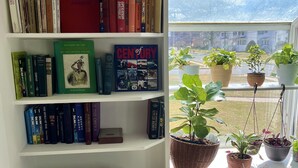 Un rincón acogedor para leer con una estantería llena de libros, un sillón cómodo y una ventana con plantas en macetas.