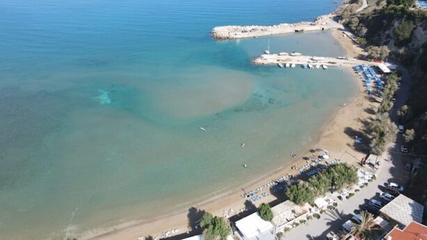 An aerial view of a coastal area with a beach, clear water, and a row of beachside buildings. - CostAnita Beach House in Almyrida (Almirida)