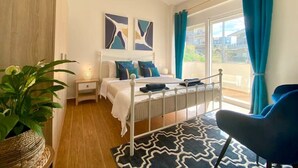 A bedroom with a bed, bedside tables, a potted plant, a chair, and a view of the outside. - CostAnita Beach House in Almyrida (Almirida)