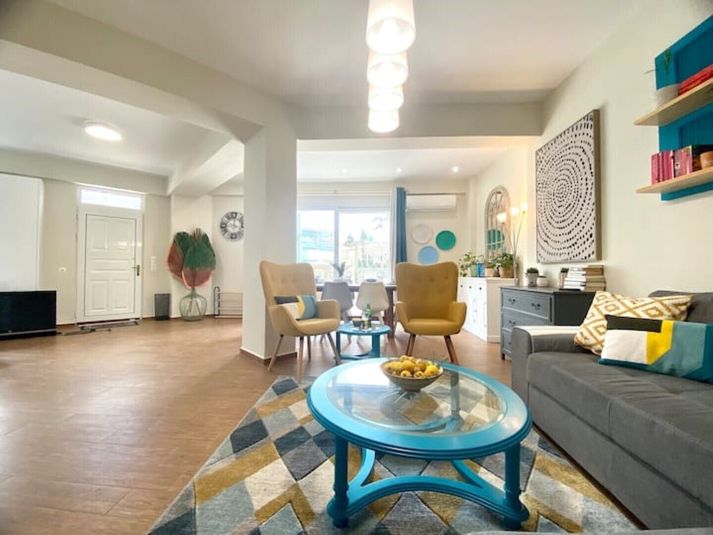 A spacious living room with a sofa, two armchairs, a glass coffee table, and a dining area with a table and chairs.