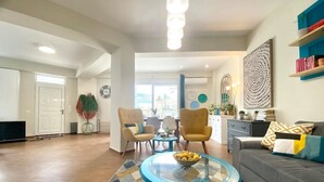 A spacious living room with a sofa, two armchairs, a glass coffee table, and a dining area with a table and chairs. - CostAnita Beach House in Almyrida (Almirida)