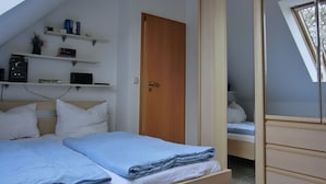 Ein Schlafzimmer mit einem Bett, einem Kleiderschrank, einem Regal mit Büchern und einem Computer sowie einem Fenster.