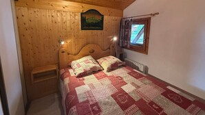 A cozy bedroom with a wooden ceiling, a bed with a quilt, a nightstand, and a window with curtains. - Les Saisies Apt, 4 pers, south balcony, near slopes (Les Saisies)