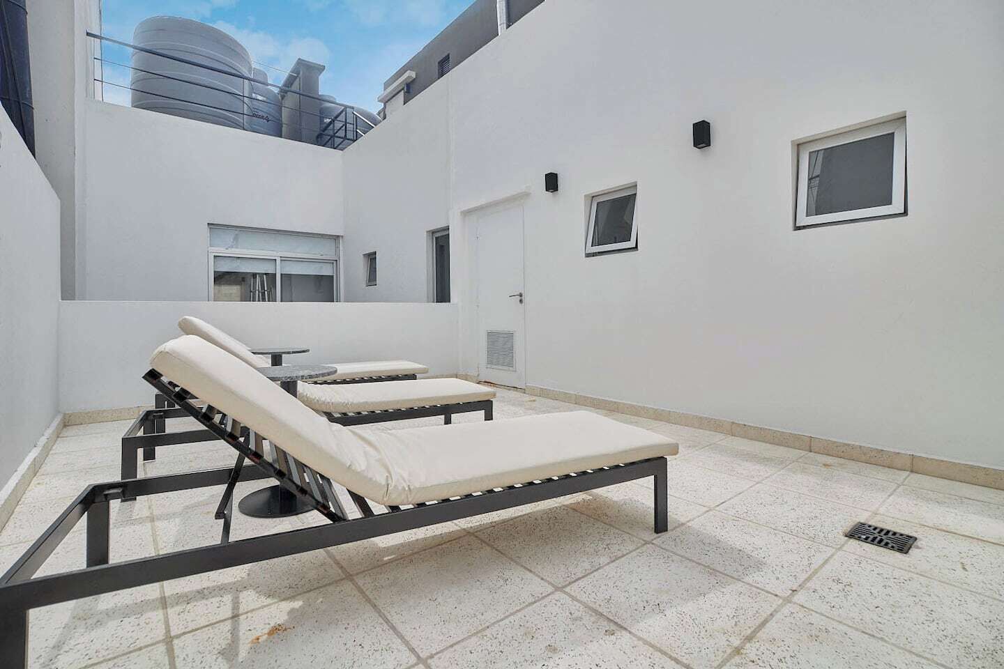 A rooftop lounge area with sunbeds and a view of industrial buildings.