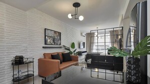 Una sala moderna con pared de ladrillo blanco, un sofá de cuero marrón, una mesa de centro negra y un gran jarrón negro con una planta.