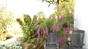 Une terrasse avec deux chaises et une table, entourée d’un mur de pierre et agrémentée de différentes plantes.