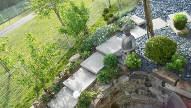 Un jardin avec un sentier en pierre, une statue et différentes plantes.