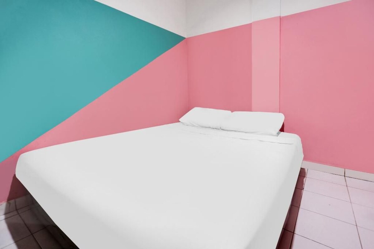 Habitación con una cama frente a una pared con un diseño geométrico en rosa y verde azulado.
