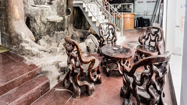 A lobby with a stone wall, a staircase, and a table with intricately carved chairs. - Hotel O Solo Baru Homestay Syariah (Batam)