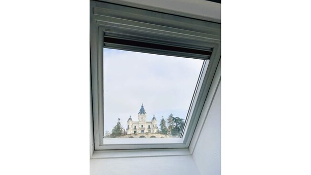 Une lucarne offrant une vue sur un grand bâtiment orné, doté de nombreuses tours et de coupoles.