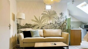 Un salon avec un canapé, une table et une fresque représentant des plantes tropicales sur le mur.